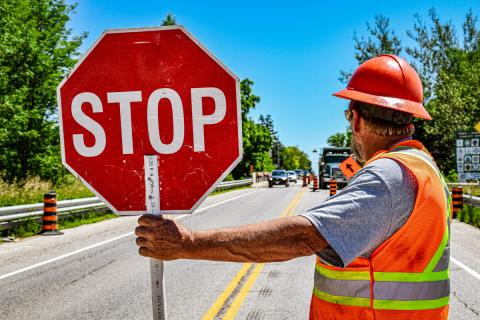 A road worker holds a stop sign while directing traffic during maintenance work on a County Road. 