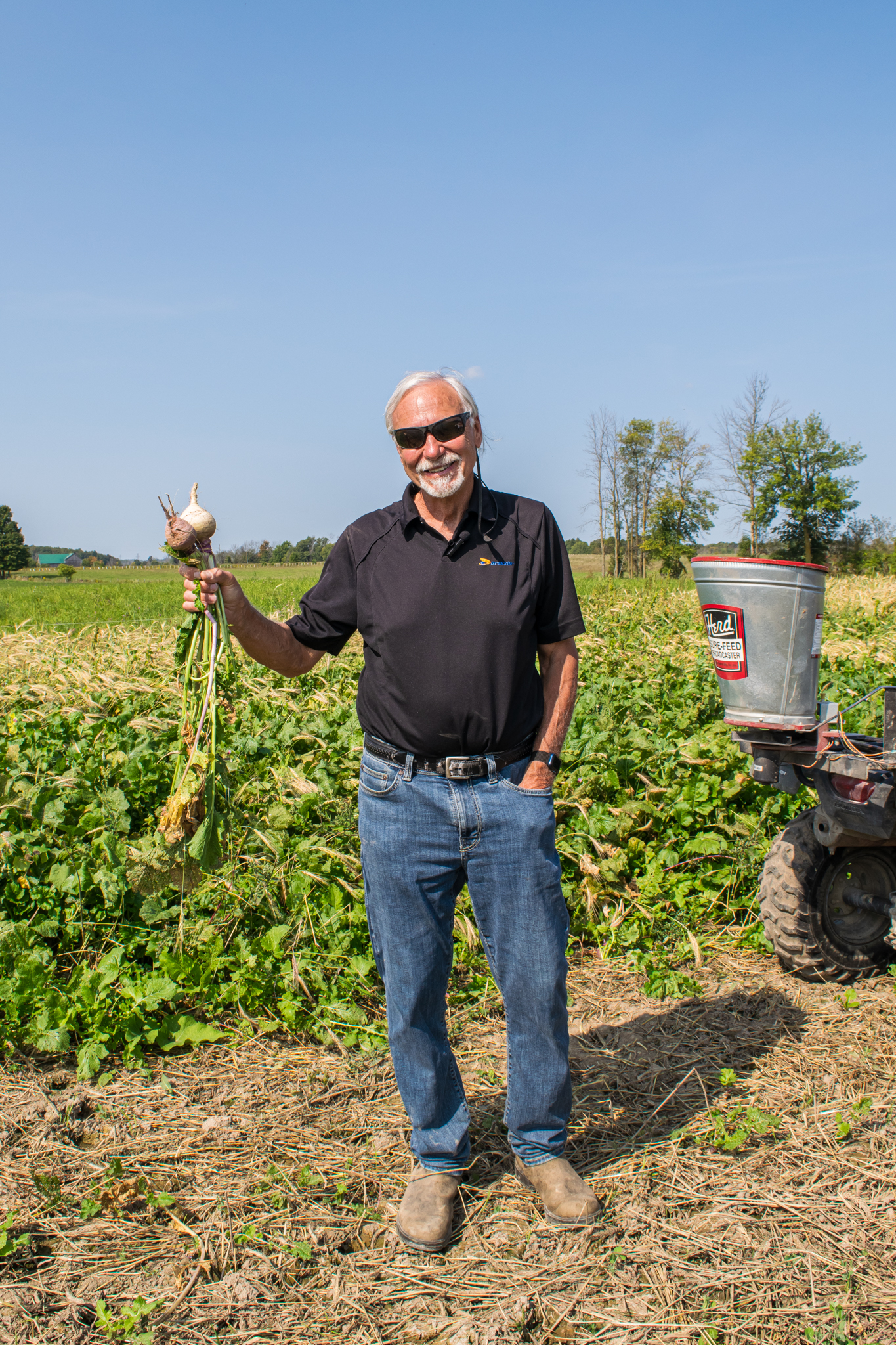 Man wearing sunglasses, standing in farm field holding a turnip