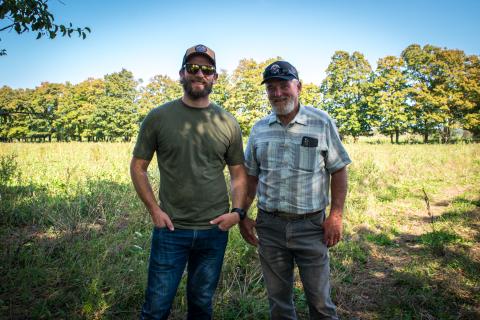Two men stand in a farm field in summer